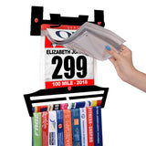 Close-up of Race Bib Holder + Medal Hanger Display Rack V2 with hand inserting race bib into vinyl sleeve, ideal for runners and athletes.